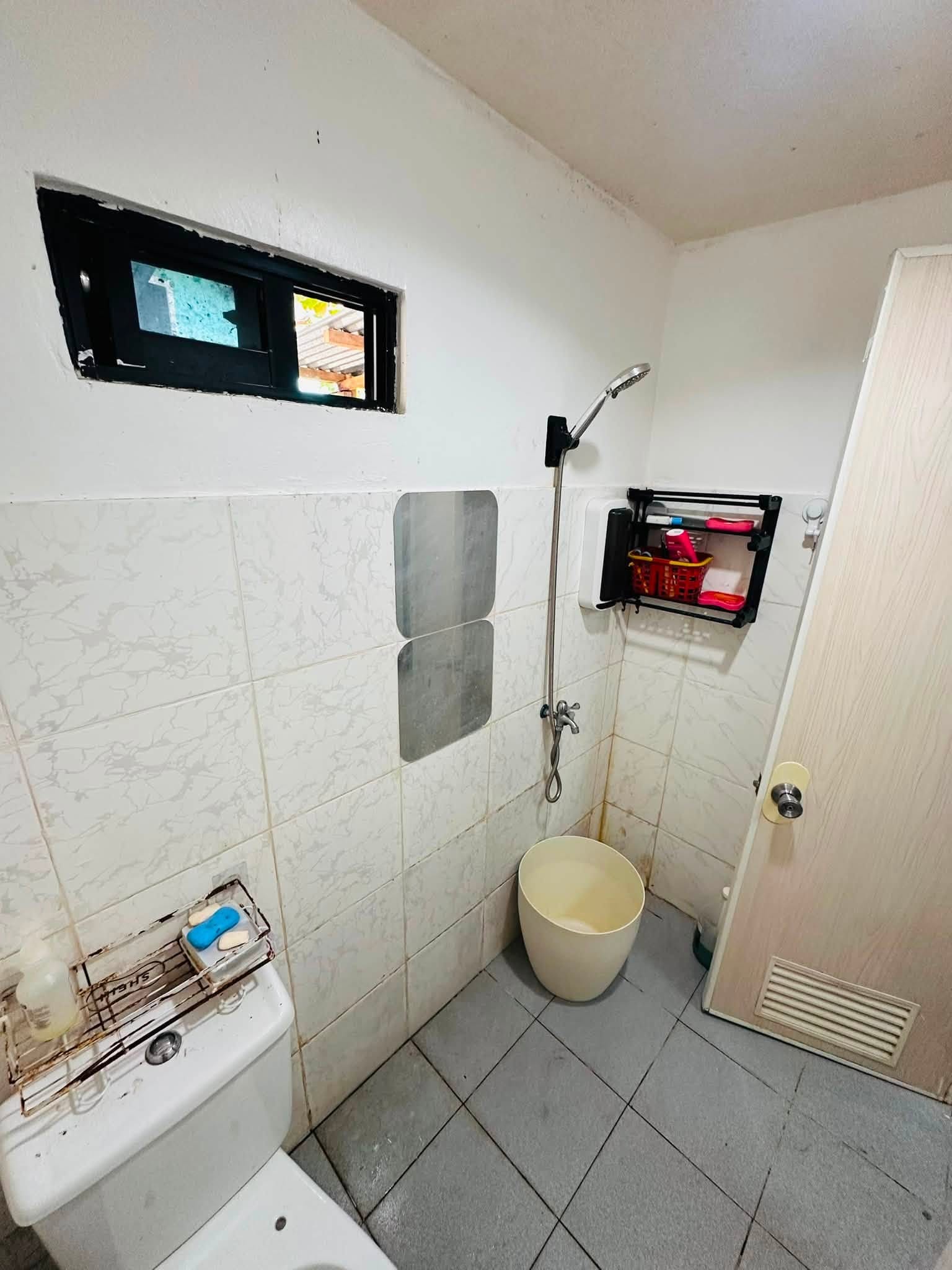 Tiled bathroom with a handheld shower, toilet and a small window to the outside