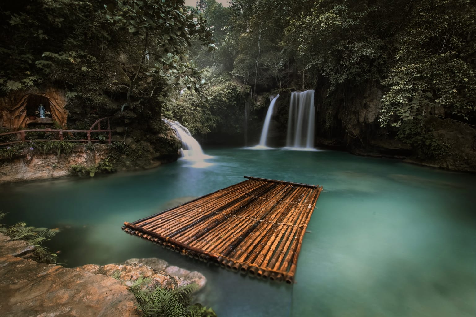 Kawasan Falls in Badian with two waterfalls dropping into a turquoise pool and a bamboo raft floating in the foreground
