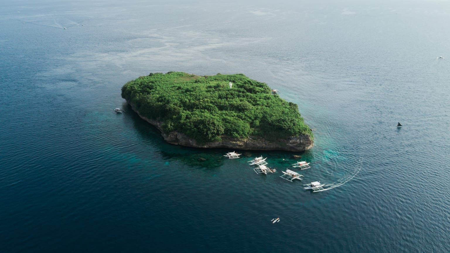 Aerial view of Pescador Island, a small green island with steep rocky sides, dive boats moored along its reef in deep blue water