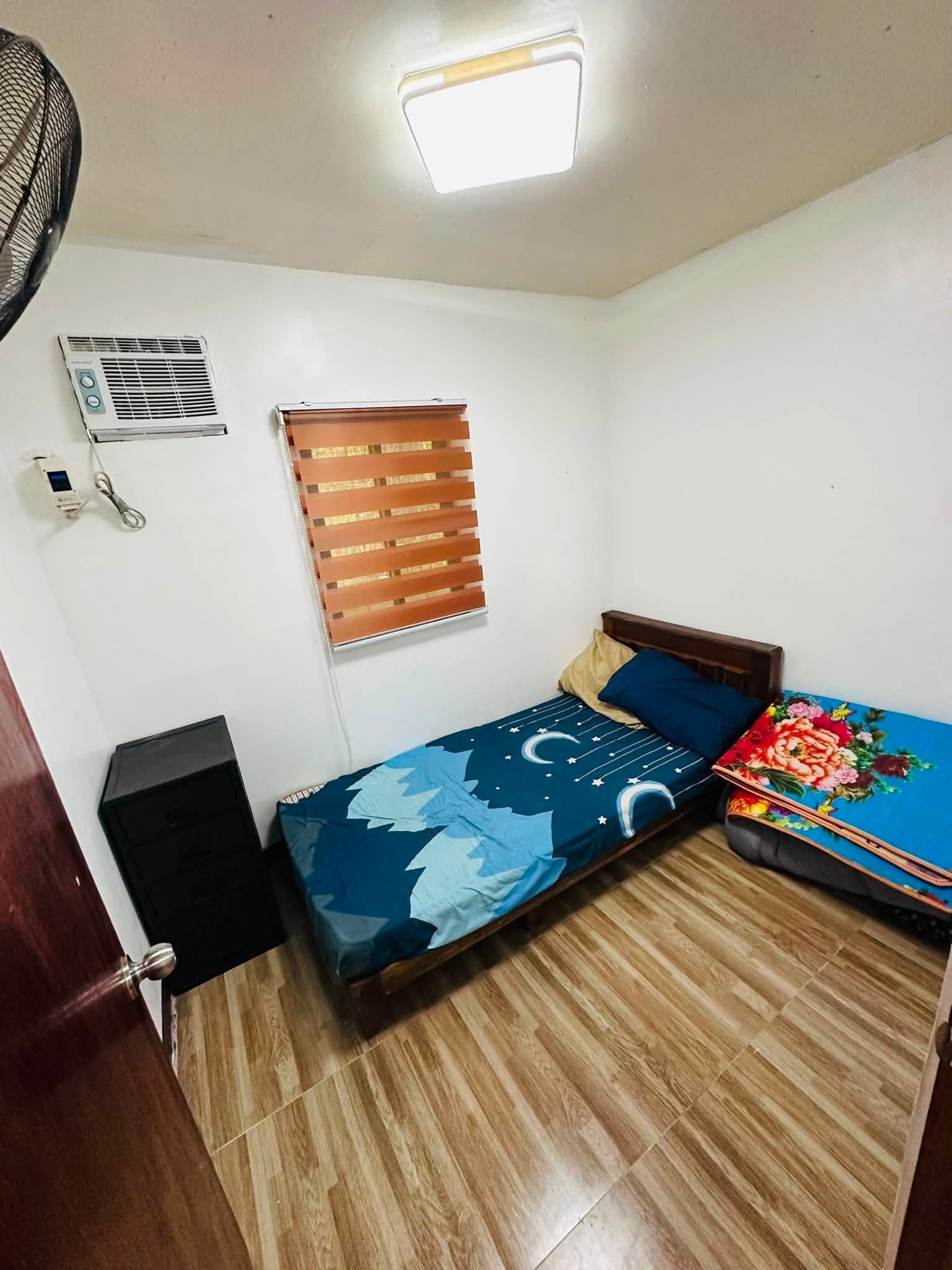Second bedroom with a double bed, wall air conditioner, wooden blinds, a small black cabinet and an extra foam mattress